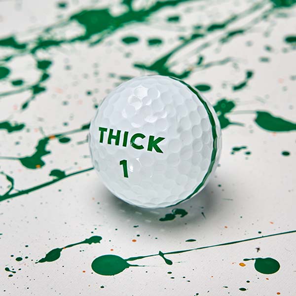 Moon Shot Pro golf ball with a green THICK 1 logo and the edge of its green stripe, on white with green paint splatter