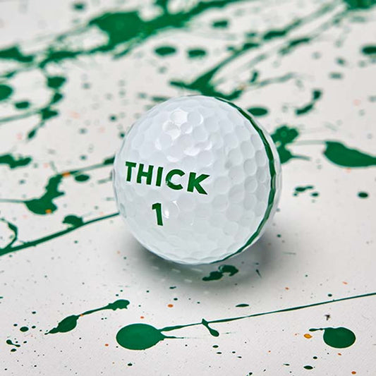 Moon Shot Pro golf ball with a green THICK 1 logo and the edge of its green stripe, on white with green paint splatter