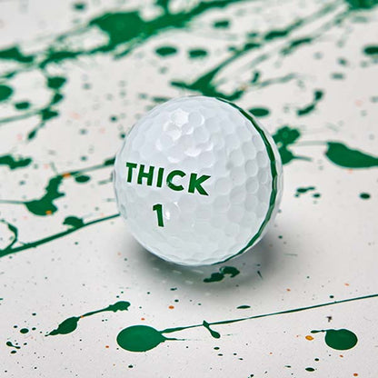 Moon Shot Pro golf ball with a green THICK 1 logo and the edge of its green stripe, on white with green paint splatter